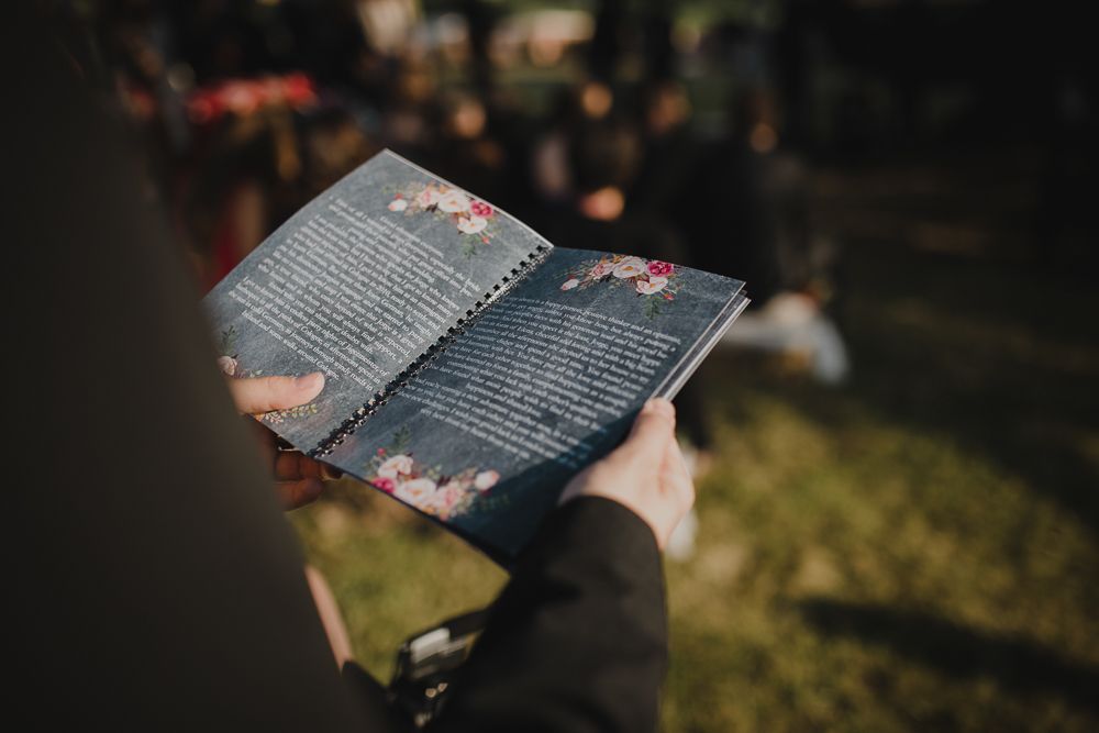 Reading from a ceremony book at an outdoor event in soft natural lighting.