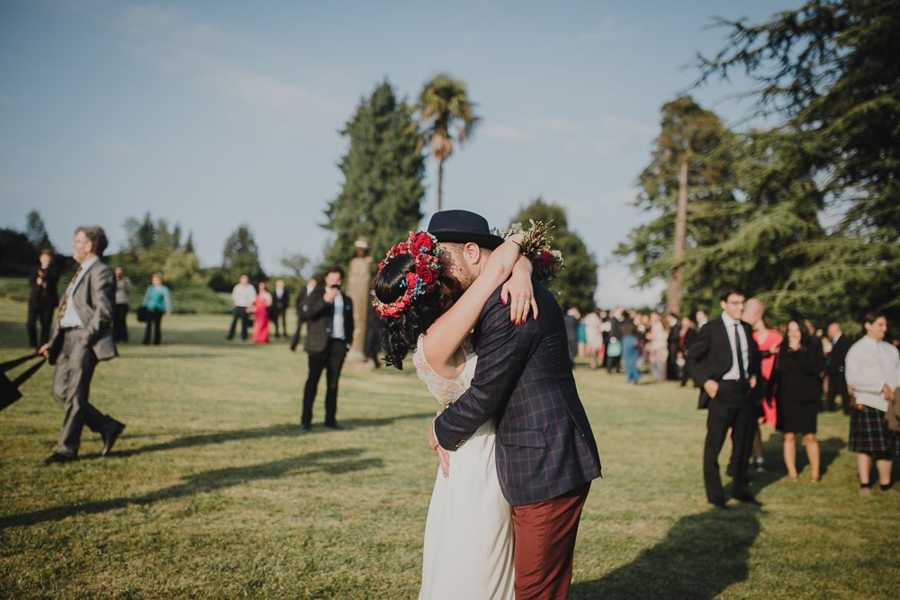 An intimate embrace during an outdoor wedding with guests looking on in the background.