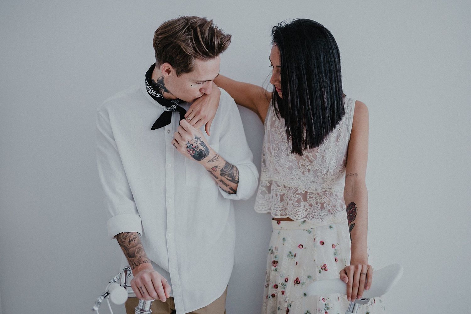 A playful moment between a couple in white outfits against a light background.