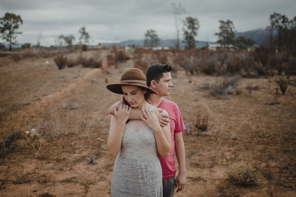 Two people explore arid desert terrain with mountains in background on overcast day.