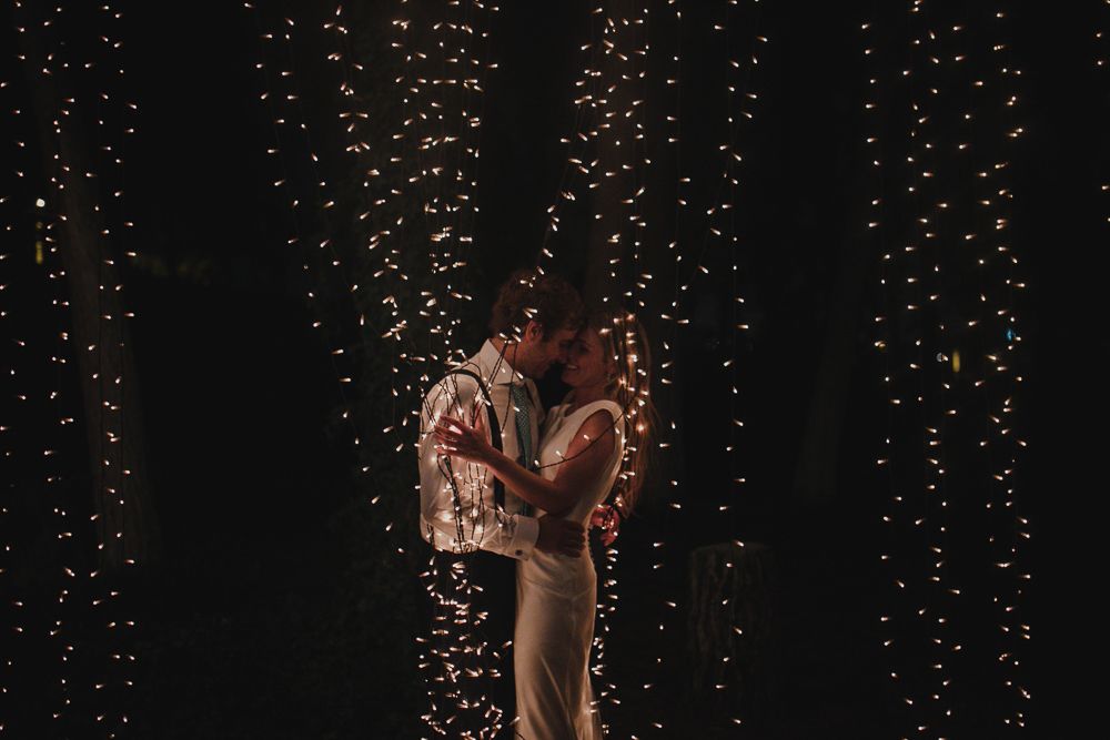 A romantic moment captured against a backdrop of vertical fairy light strands creating a magical ambiance.