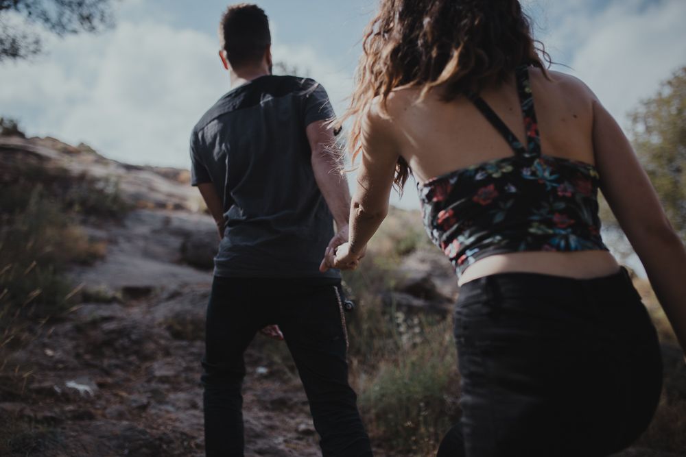 Two people hiking on a desert trail with backpacks against blue sky.