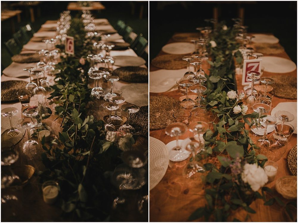 Rustic wedding table setting with greenery garland runner and glowing candlelight.