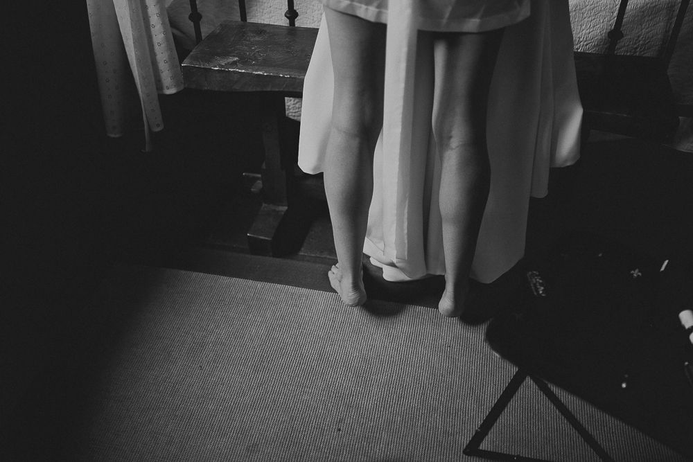 Black and white view of feet and the bottom of a robe standing on dark flooring.