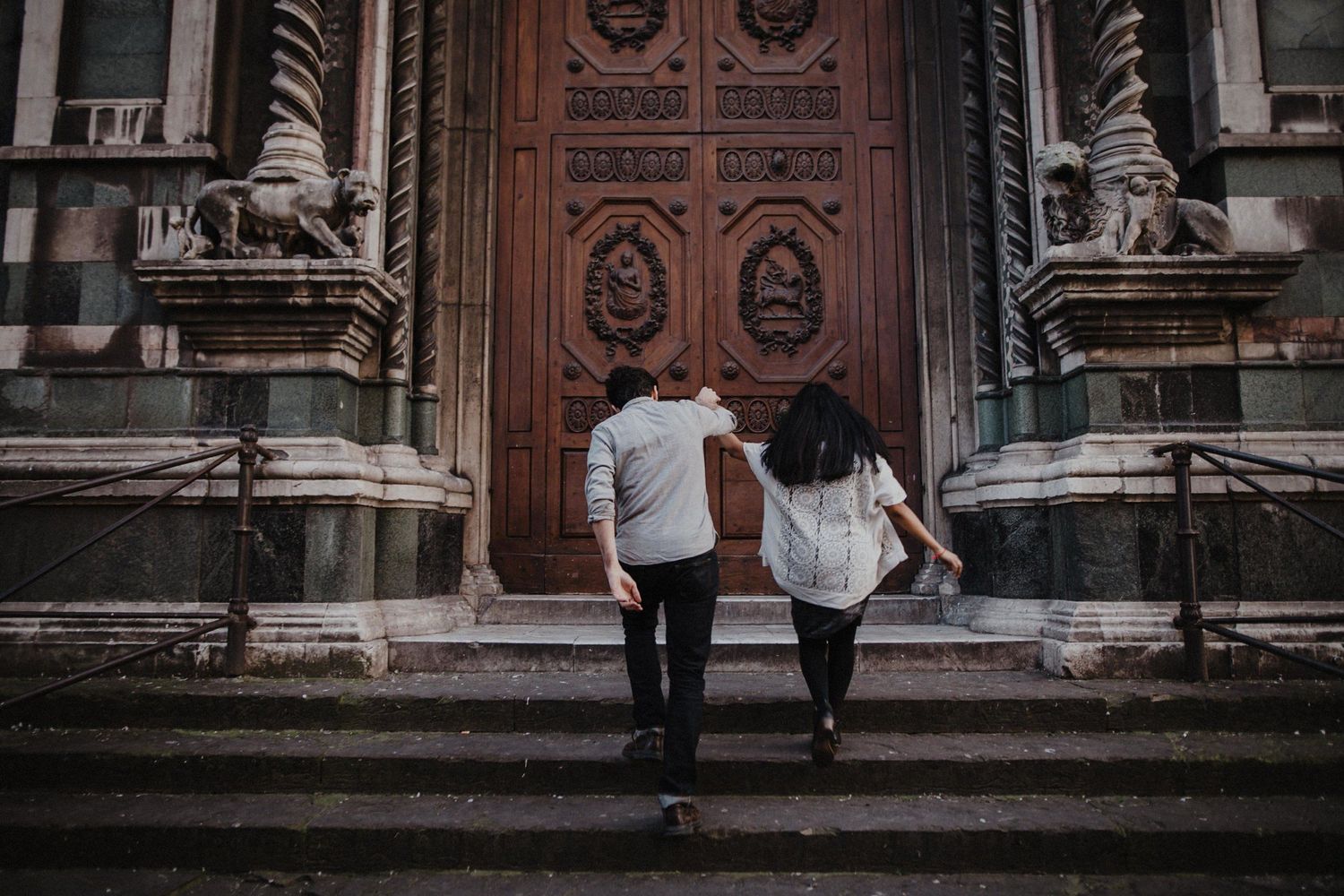 Couple ascending stone steps towards grand cathedral entrance in romantic setting.