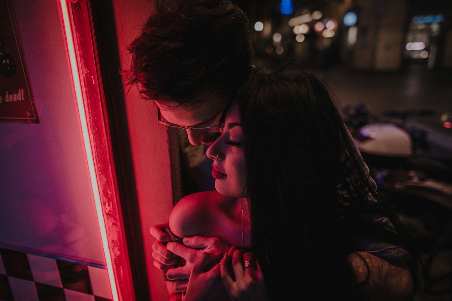 A couple bathed in red neon lighting share an intimate moment.