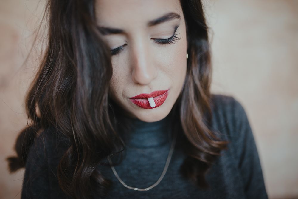Close-up portrait with red lipstick and delicate necklace against neutral background.