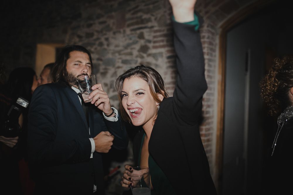 Guests celebrate and dance together at a lively party in a rustic brick-walled venue.