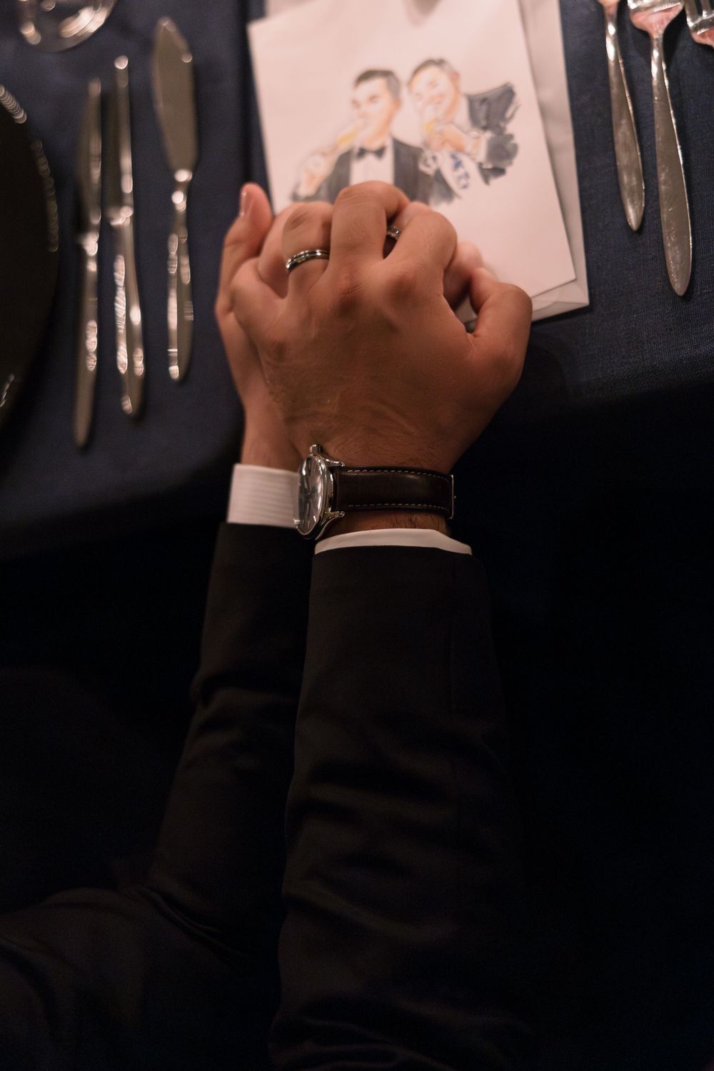 Close-up of clasped hands wearing formal attire at a wedding reception.