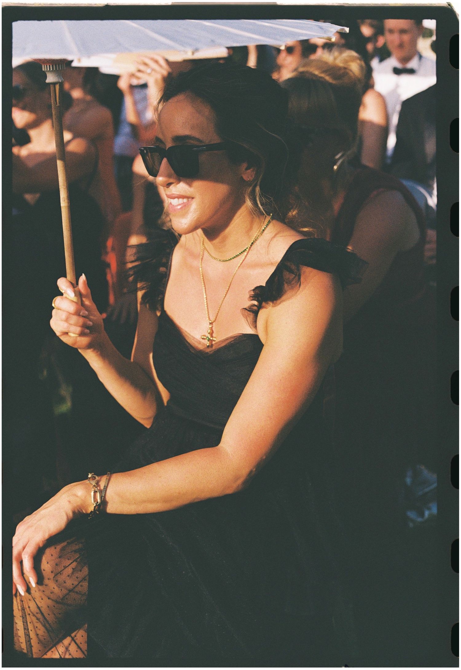 Wedding guest in black dress with sunglasses enjoying outdoor celebration.
