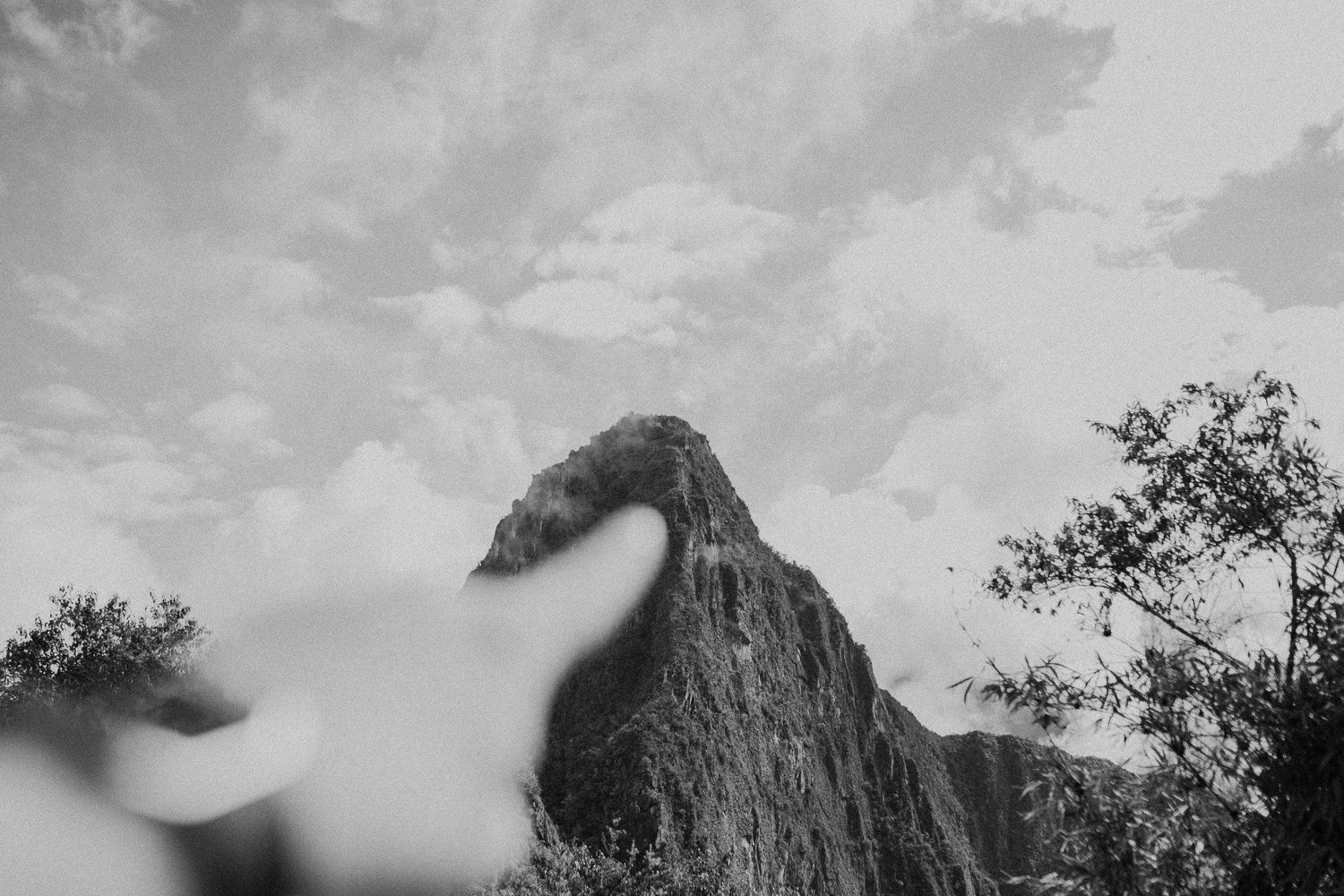 Dramatic black and white silhouette of a mountain peak emerging through clouds against a moody sky.