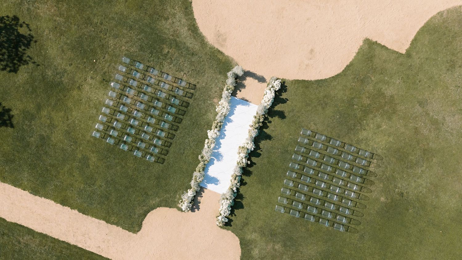 Aerial view of an elegant outdoor wedding ceremony setup with white chairs arranged symmetrically on green lawn.