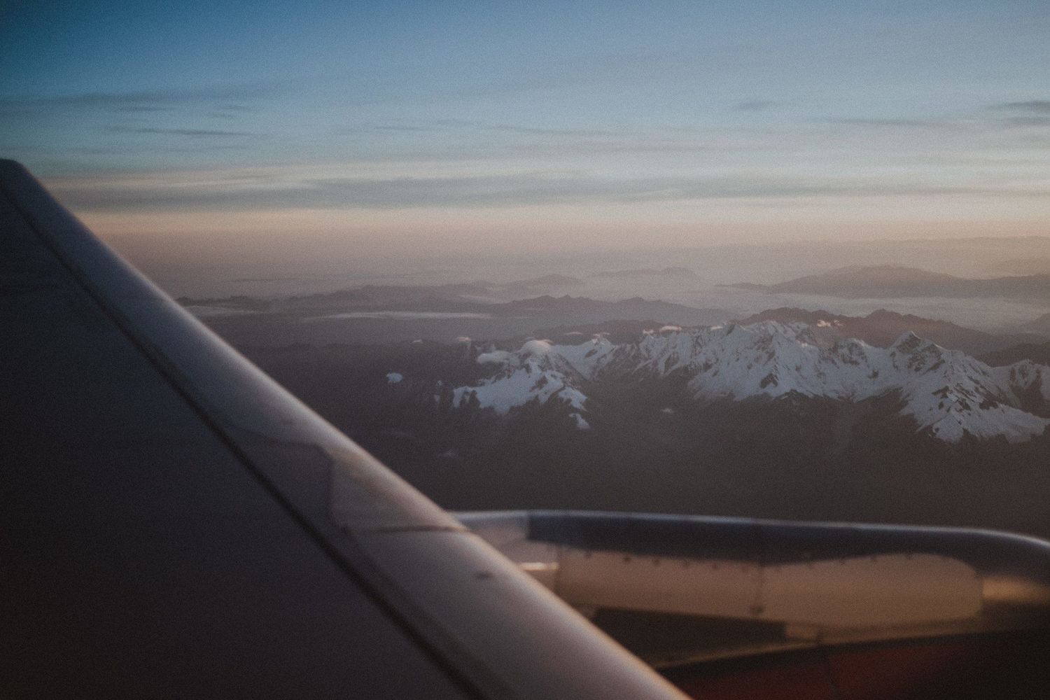 View from airplane window showing snowy mountain peaks during sunset or sunrise.