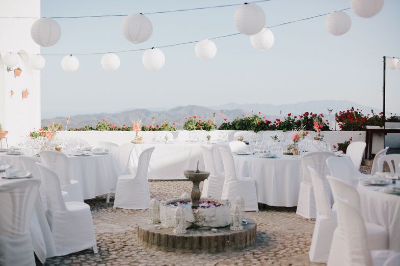 An elegant outdoor wedding reception setup with white-covered tables and chairs under string lights at dusk.