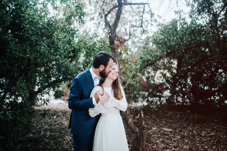 A romantic wedding couple embraces in a lush garden setting with soft natural lighting.
