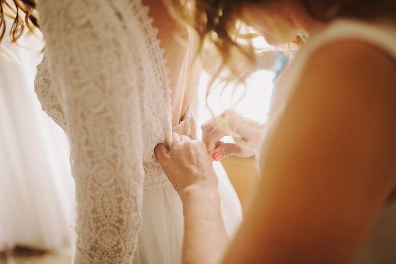 Close-up detail of intricate lace wedding dress being fastened in warm sunlight.