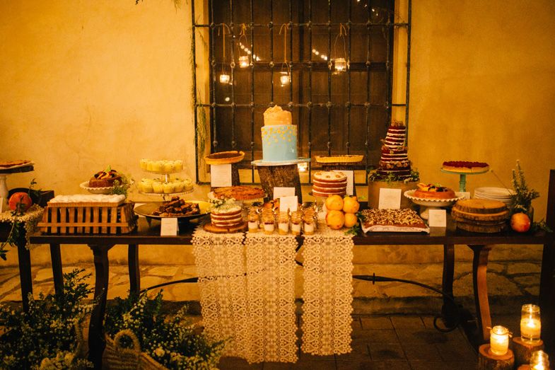 Elegant wedding dessert table with multiple cakes and treats illuminated by candlelight.