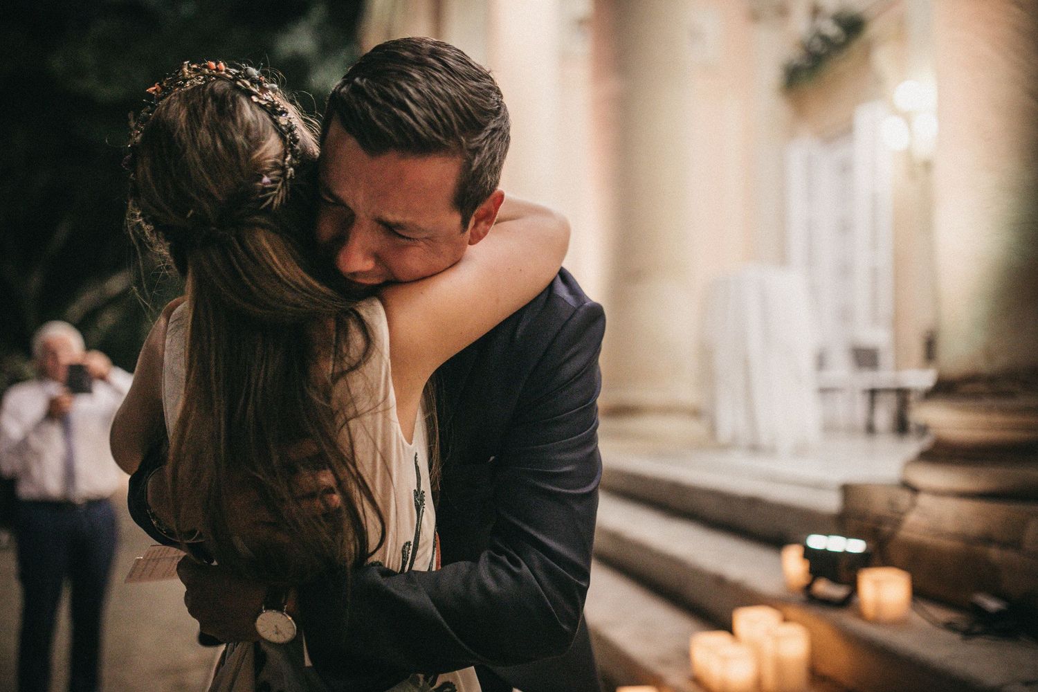 A romantic embrace at an elegant venue with candlelight and classical columns in the background.