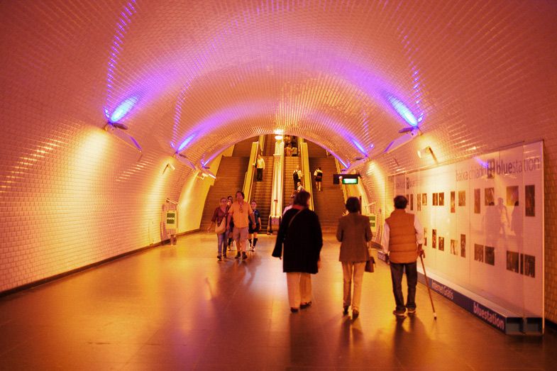 Illuminated curved tunnel corridor with purple lighting and art gallery displays.