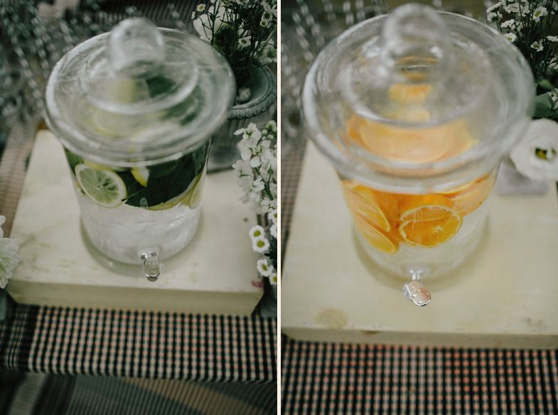 Two elegant glass drink dispensers with citrus fruits on checkered tablecloth.