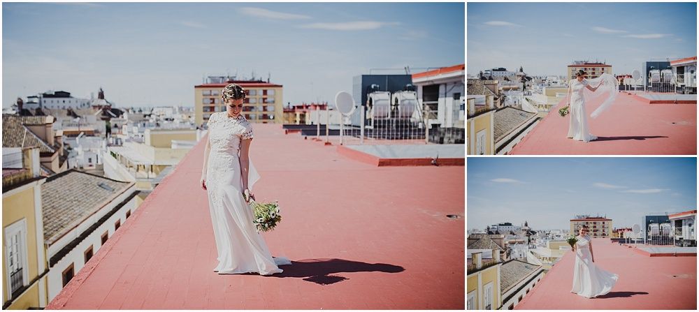 Bride in flowing white dress walking on pink rooftop with city buildings in background.