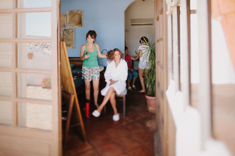 People gathered in a rustic hallway with terracotta floors and white walls during wedding preparations.