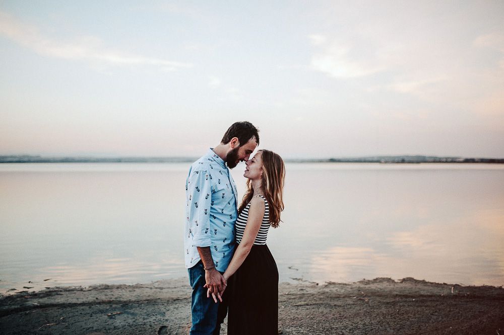 Romantic couple embracing on beach with calm water in background.