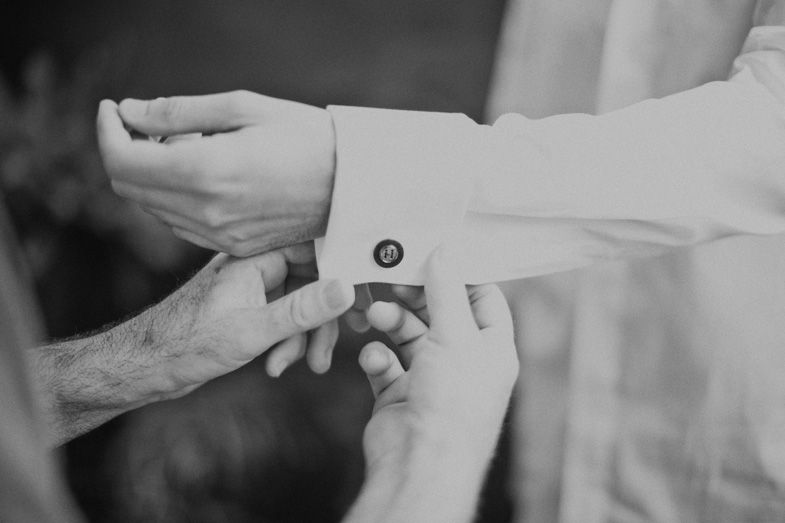 Hands helping with cuff links during formal dressing preparation.
