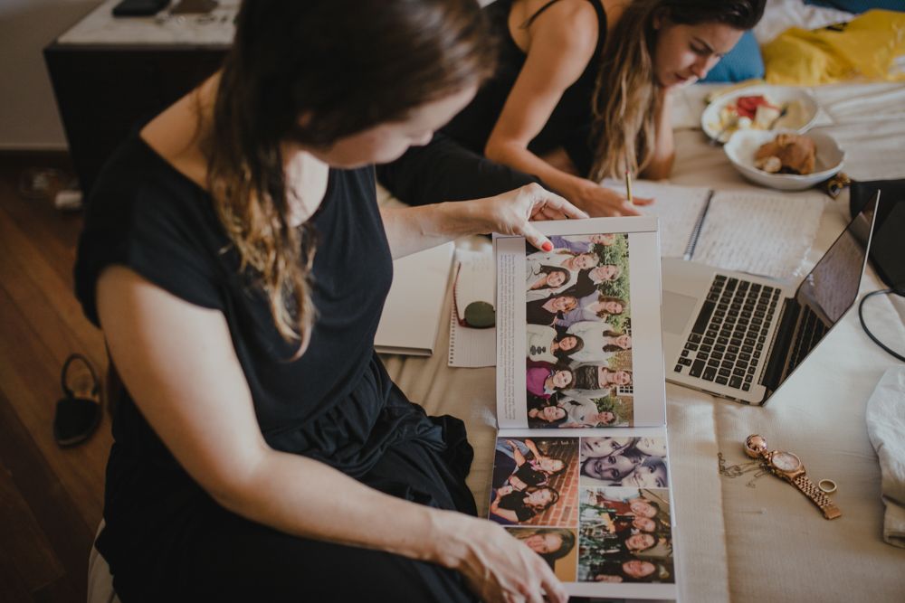 Woman in black dress looks through photo album with laptop on desk.
