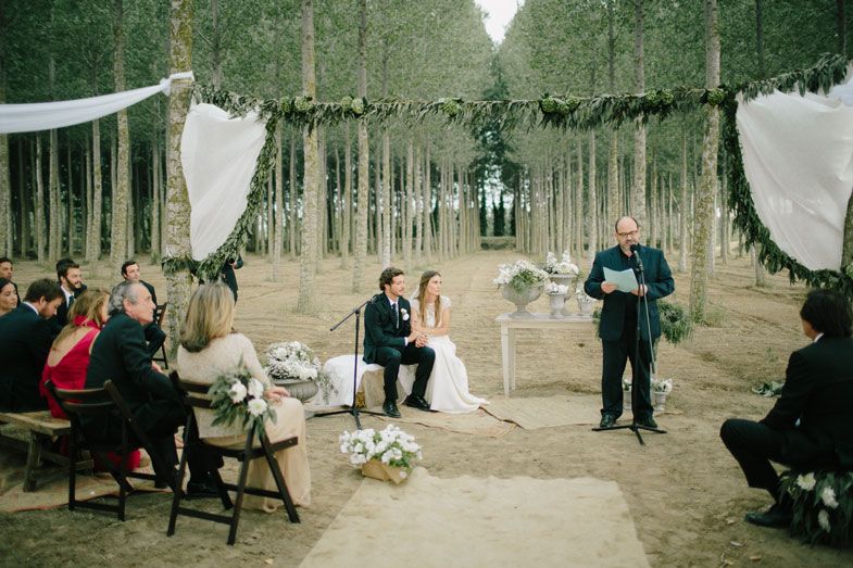 An intimate forest wedding ceremony with white drapes and greenery decorations among tall aspen trees.