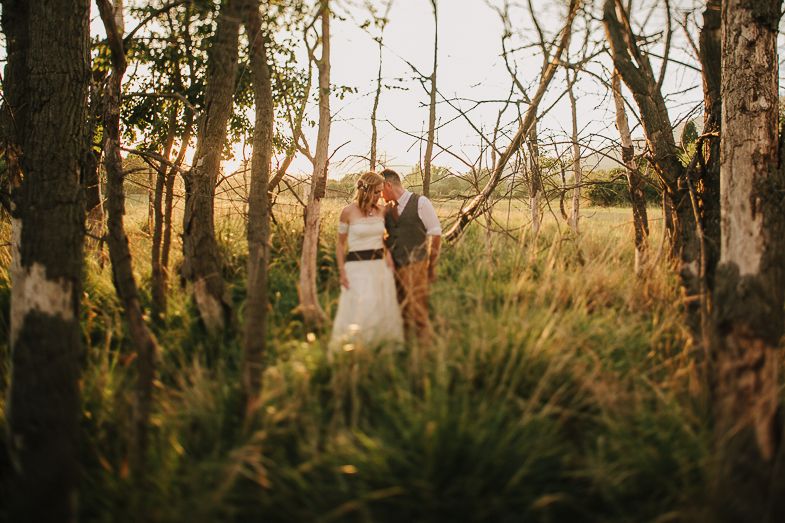 Wedding couple standing among trees in a natural woodland setting.