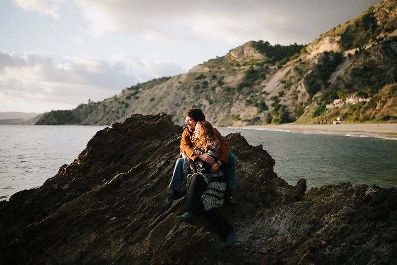 Couple sitting together on coastal rocks during golden hour with ocean views.