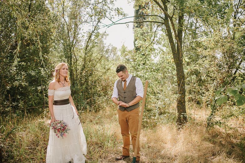 Couple in rustic wedding attire standing together in dappled sunlight.