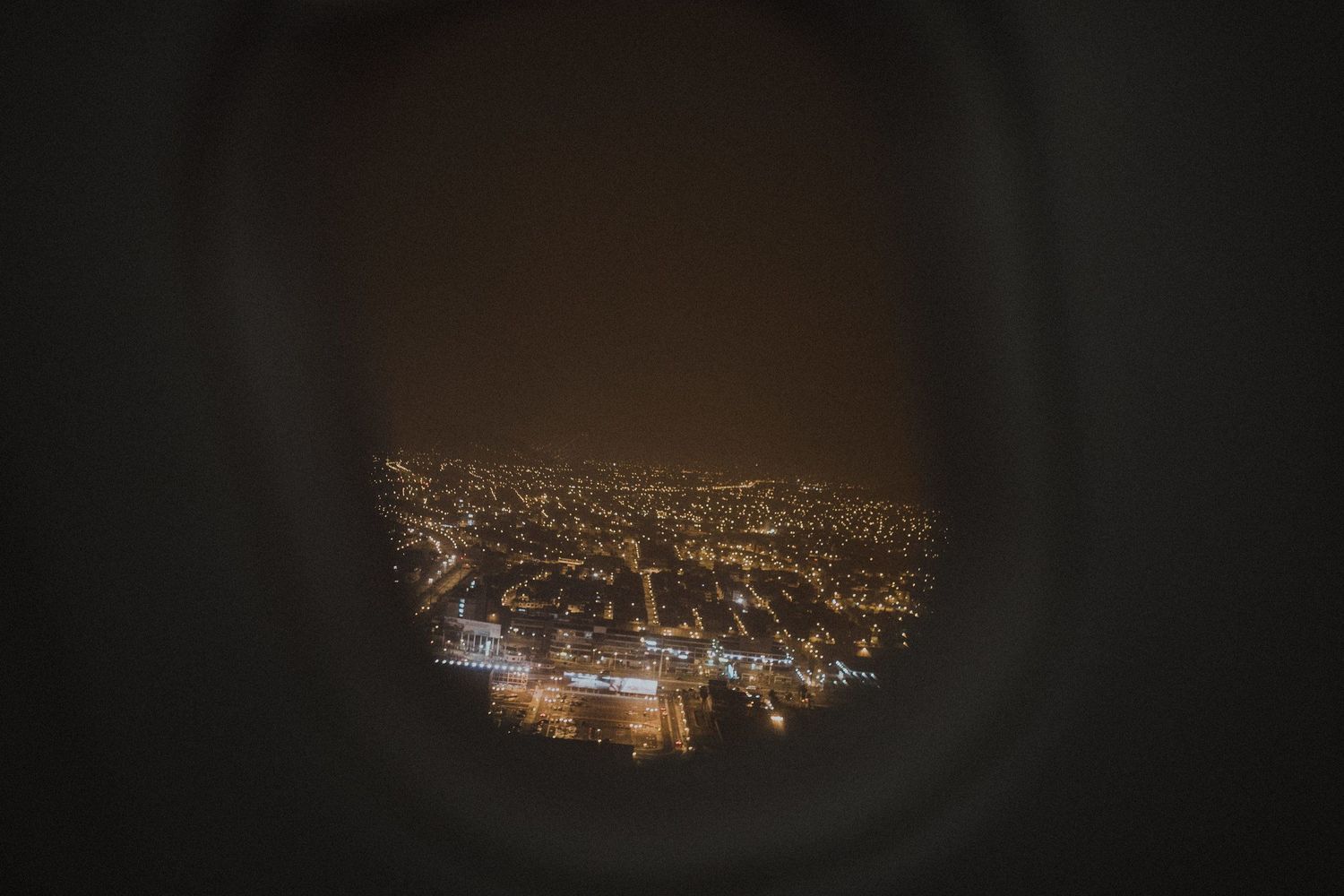 Aerial cityscape view at night through a circular frame showing glowing lights across an urban landscape.