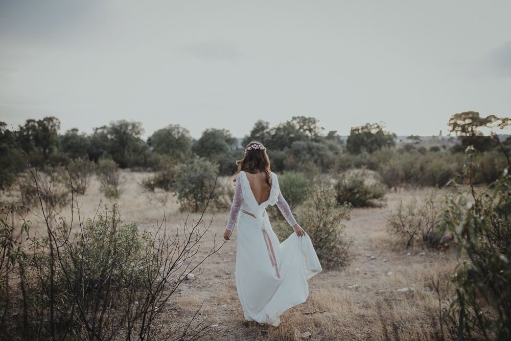 Woman in flowing white dress walking through desert landscape.