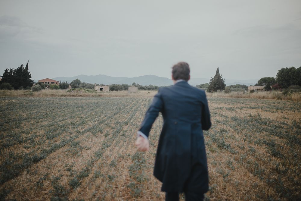 Back view of person in navy coat walking through rural field.
