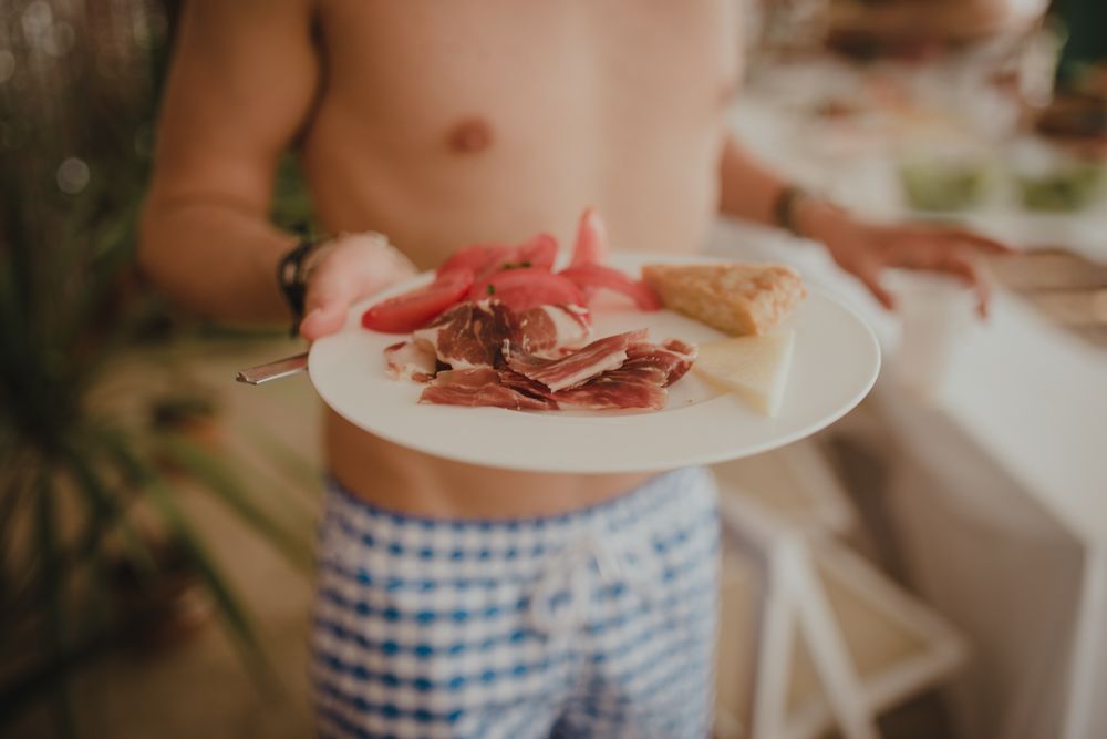 Hand holding a plate with charcuterie and fresh meat selections.