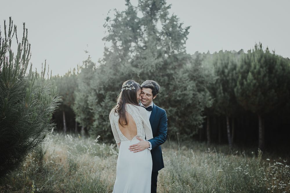 A couple in wedding attire embraces in a misty mountain field at dusk.