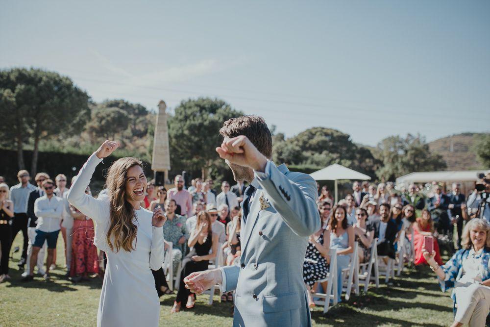 Wedding celebration on sunny lawn with crowd of guests cheering in background.