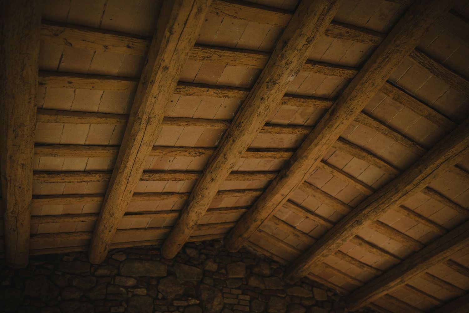 Rustic wooden ceiling beams in a dark attic space create a geometric pattern of shadows and lines.