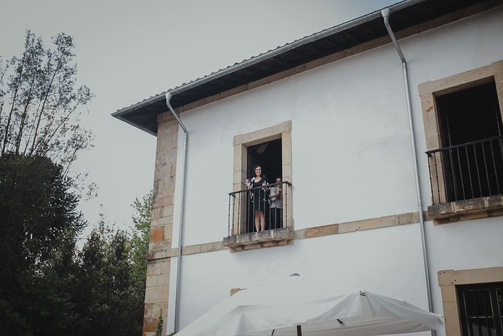 A white stucco building with a couple standing at a second-floor window.