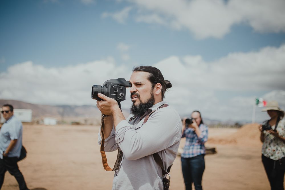 Photographer with a camera taking photos in a desert setting with people in the background.