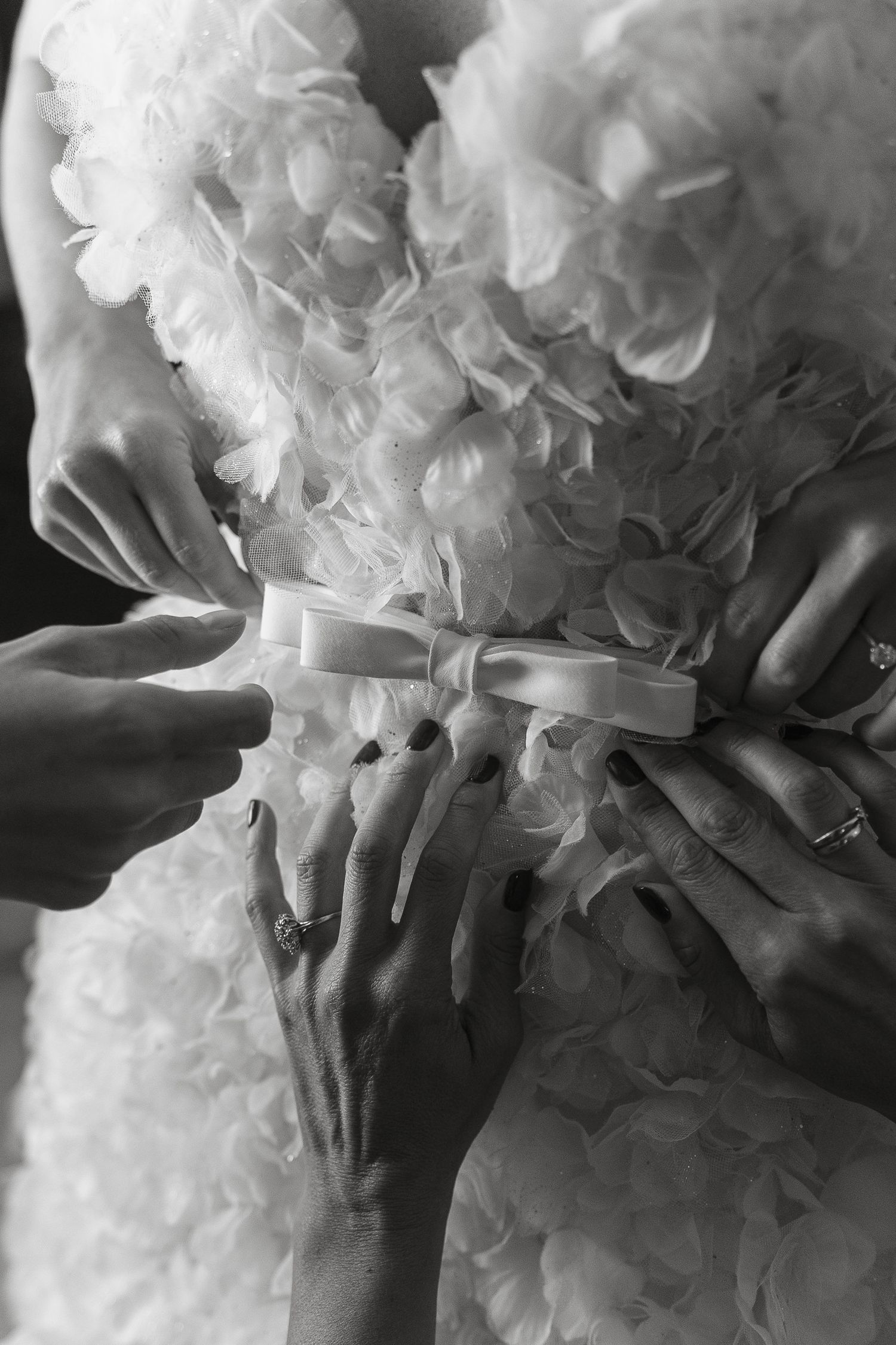 Close-up of hands adjusting ornate details on ruffled wedding dress.