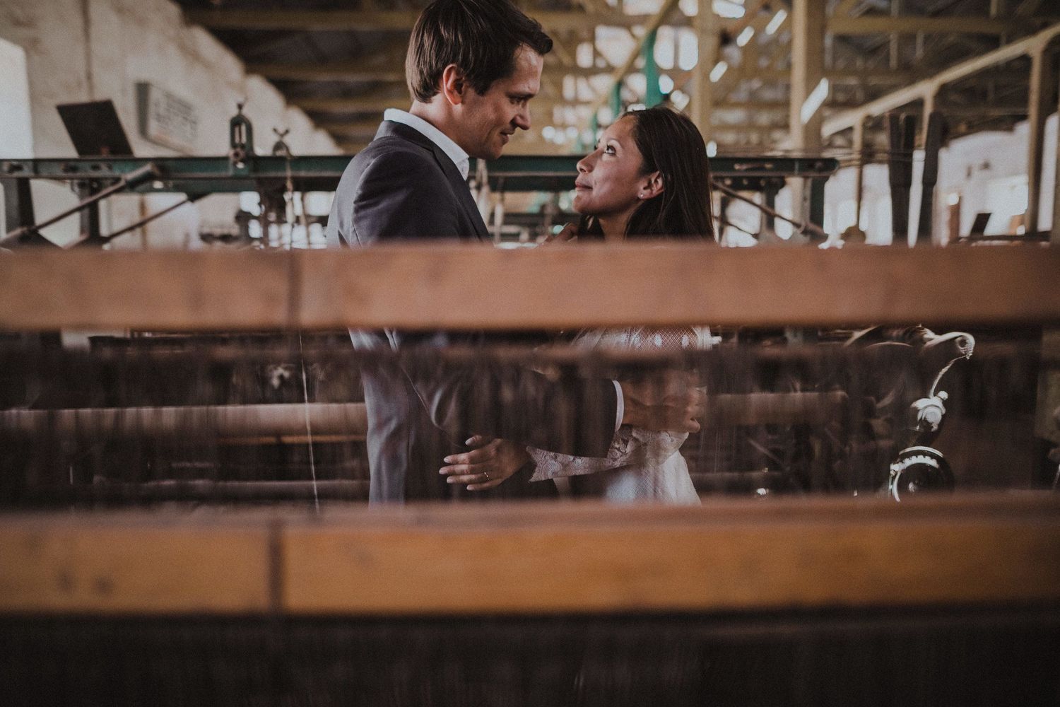 Couple shares an intimate moment framed by industrial equipment in a vintage warehouse setting.