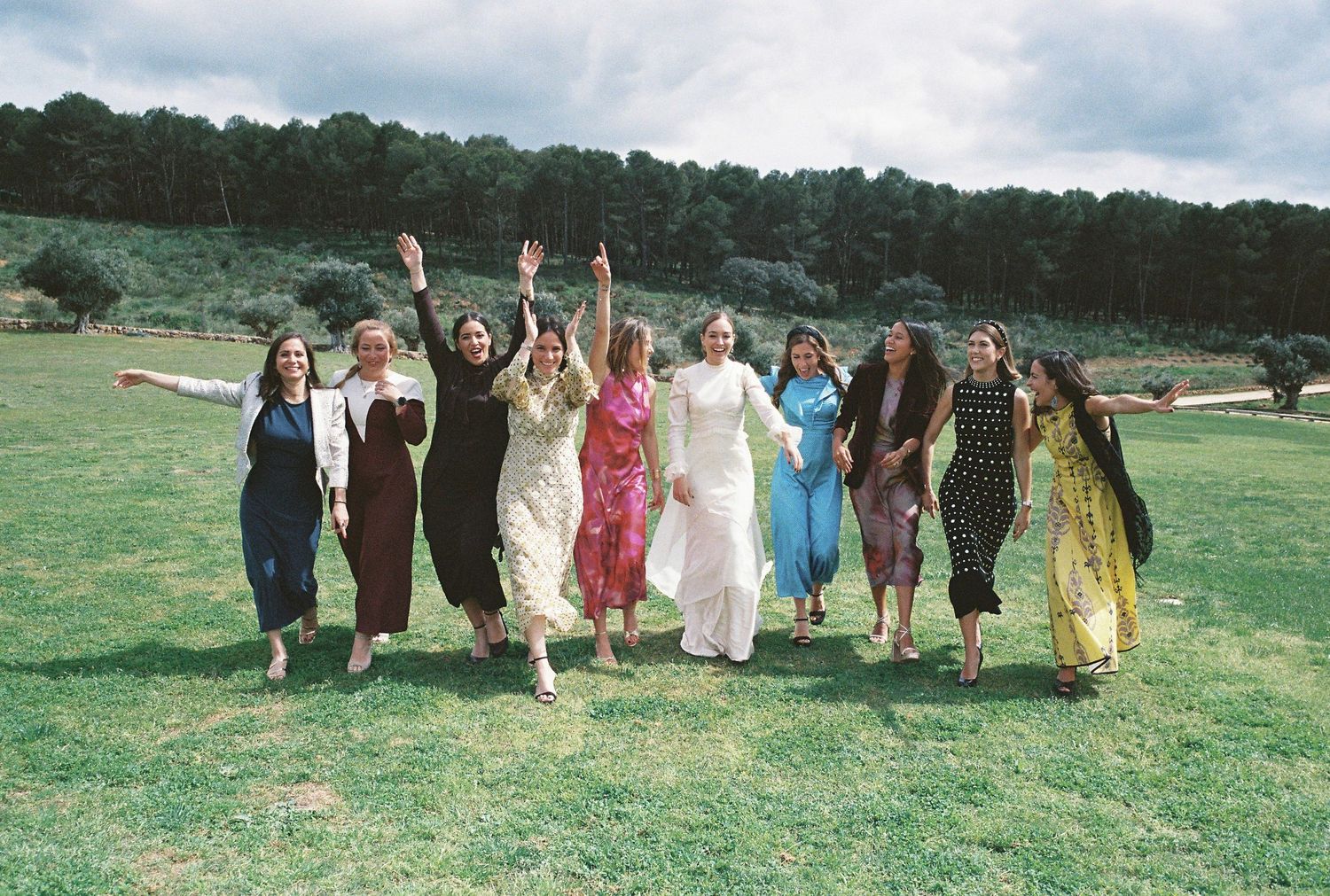 A panoramic sequence shows a group in colorful dresses running and jumping joyfully across a green hillside meadow.