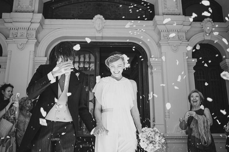 Black and white photo of newlyweds exiting venue under shower of confetti.