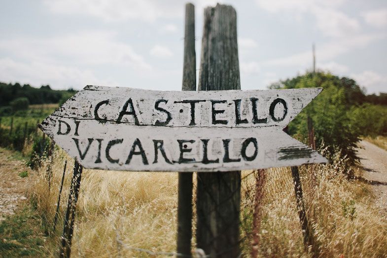 Rustic wooden sign reading Castello di Vicarello in an Italian countryside setting.