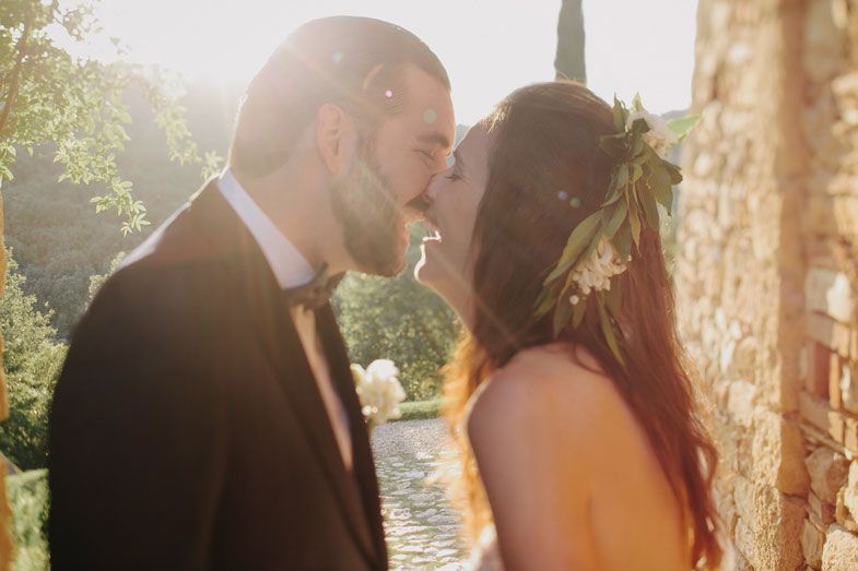 A tender wedding kiss captured in warm sunlight with cypress trees in background.