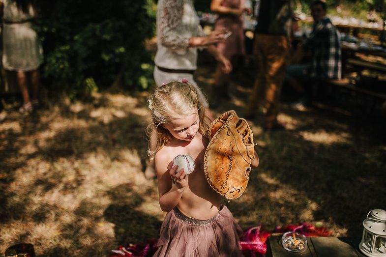 A small child in a pink dress plays with toys at an outdoor wedding reception.