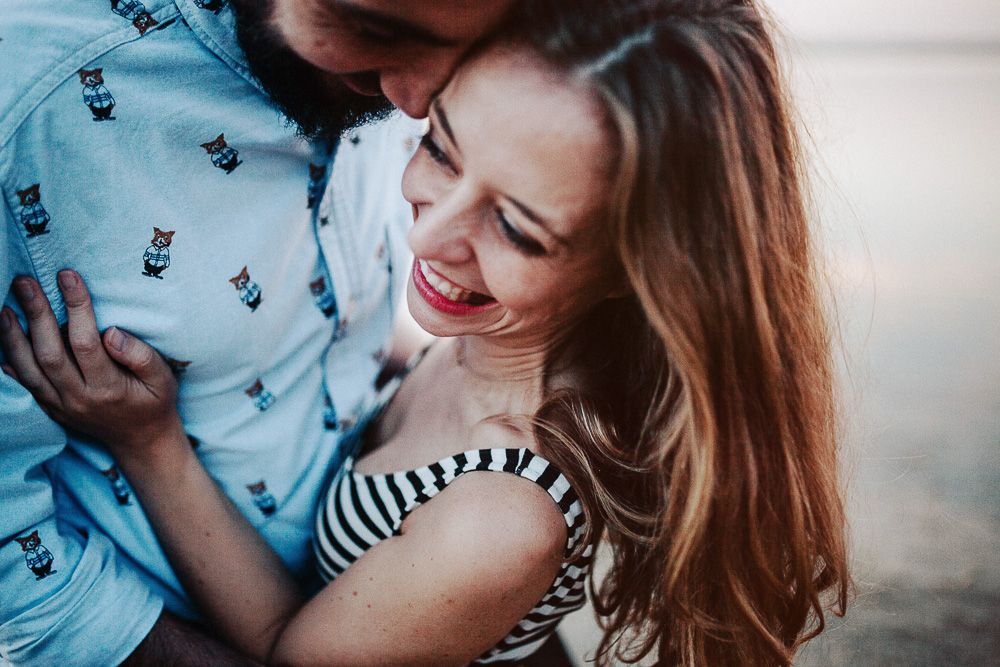A joyful couple laughs together during a waterfront photoshoot.